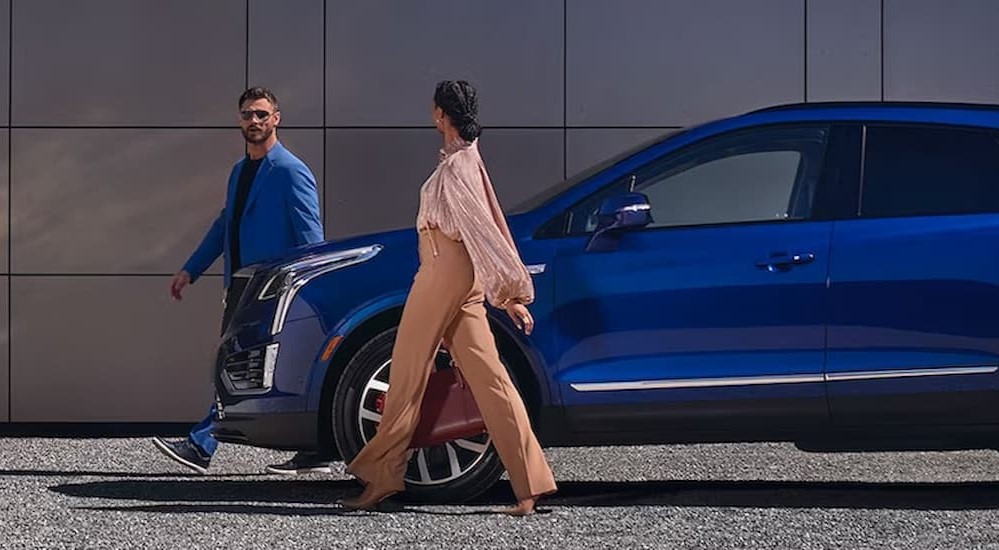 Two people are shown walking away from a parked blue 2024 Cadillac XT5.