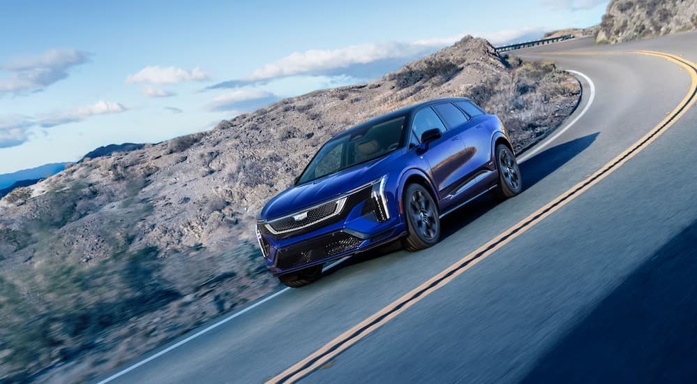A blue 2026 Cadillac OPTIQ-V driving on a highway.