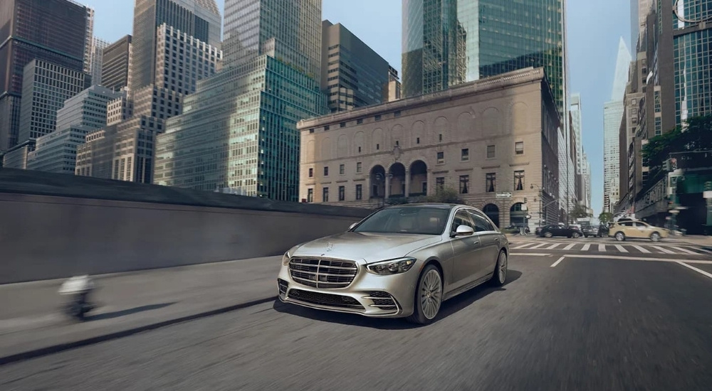 A silver 2023 Mercedes-Benz S-Class driving in a city.