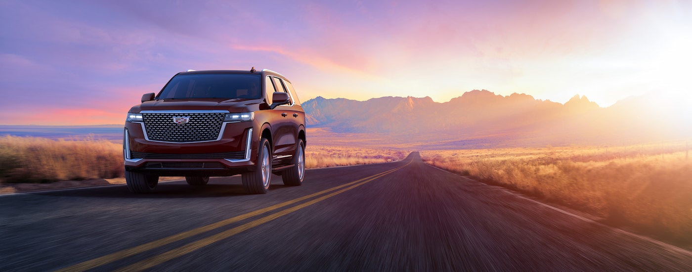 A red 2024 Cadillac Escalade driving away from mountains at sunset.