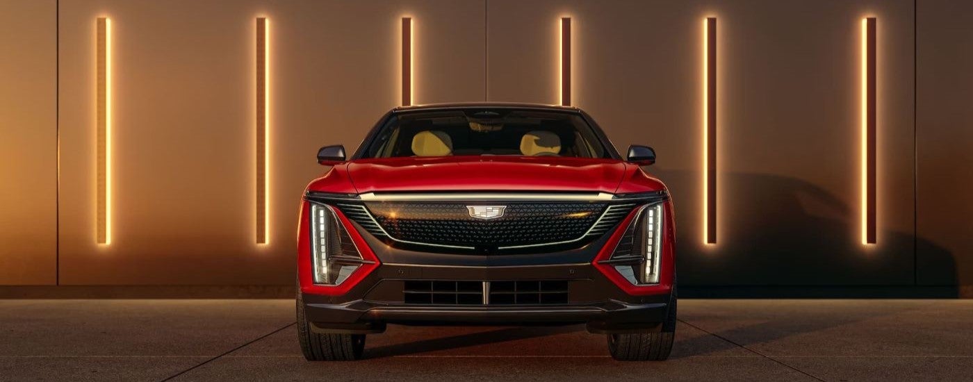 A red 2024 Cadillac LYRIQ for sale is shown parked near a modern wall.