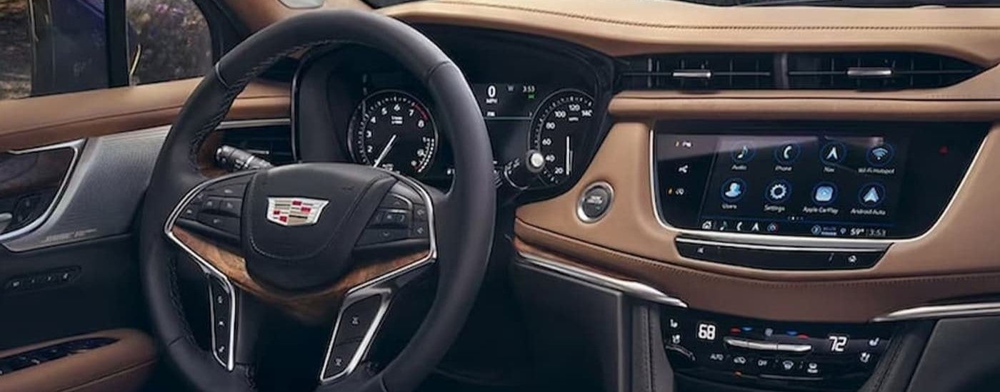A steering wheel and dashboard are shown in the black and brown interior of a 2024 Cadillac XT5.