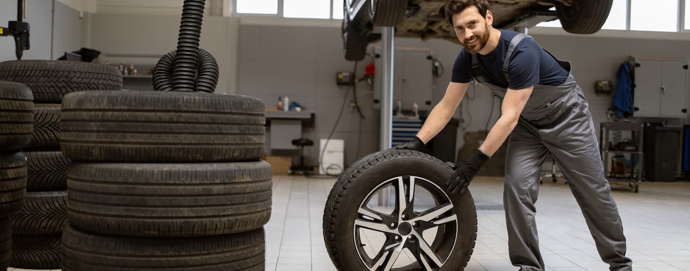 Mechanic rolling a tire towards a stack.