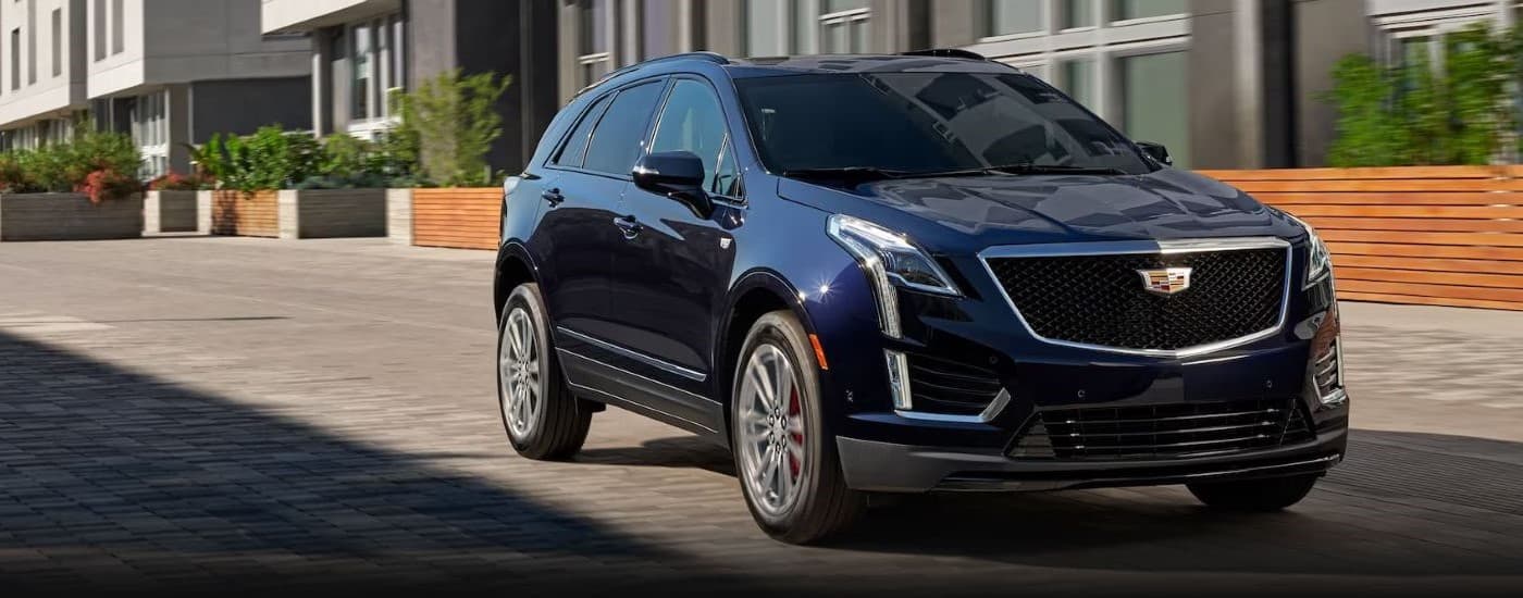 A dark blue 2023 Cadillac XT5 driving from a dealer with a used Cadillac for sale.