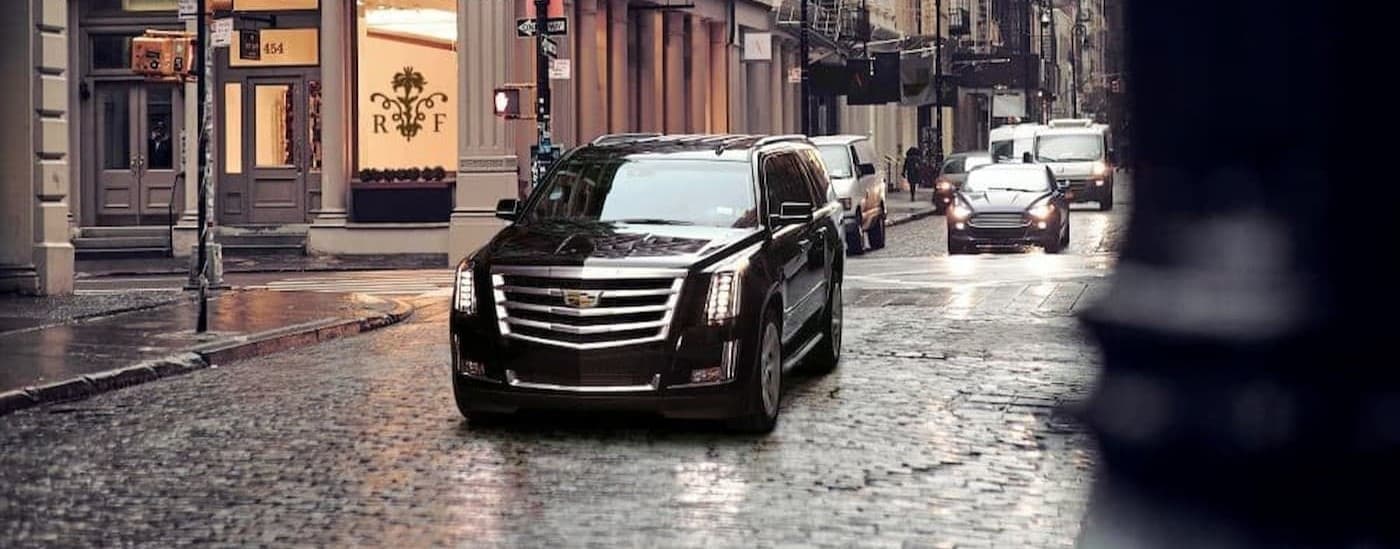 A black 202 Cadillac Escalade driving in a city.