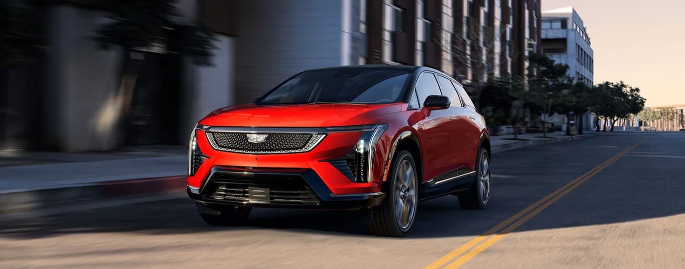 A red 2026 Cadillac OPTIQ-V driving to a car dealership near Milford.